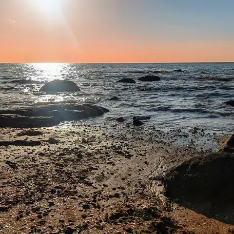 Rocky shoreline at sunset, with golden light reflecting off the sea and scattered pebbles on the sandy beach