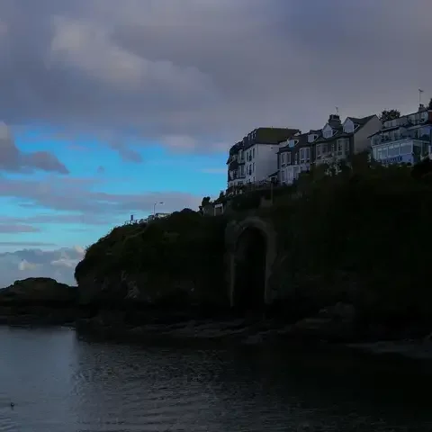 Silhouette of coastal houses on a cliff at dusk with a calm sea and cloudy sky