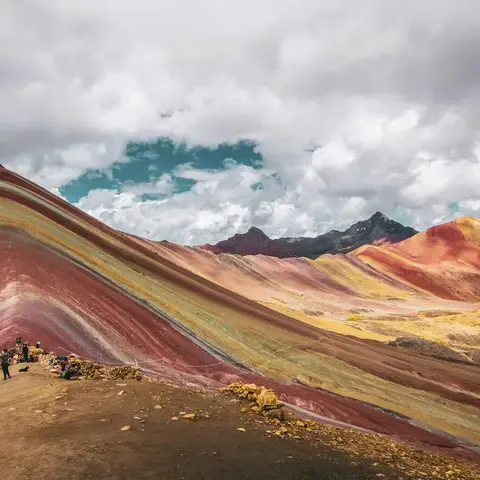 Vivid Rainbow Mountain in Peru, showcasing stunning layers of red, yellow, and green hues under a dramatic cloudy sky