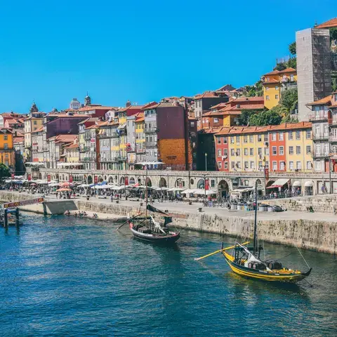 Colorful riverside houses and traditional boats in Porto, Portugal, along the scenic Douro River under a bright blue sky