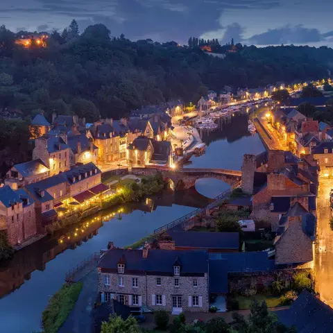 Charming medieval village at night, with illuminated streets, stone houses, and a peaceful river reflecting the warm lights