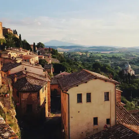 Sunlit Tuscan village with rustic terracotta rooftops, rolling green hills, and a scenic view of a distant church