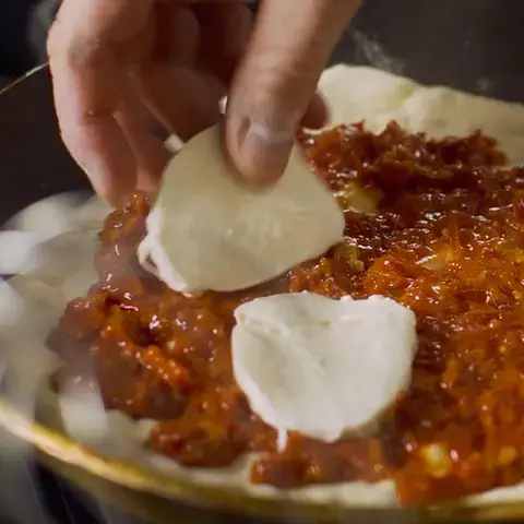 Hand placing slices of mozzarella on pizza dough with tomato sauce in a frying pan