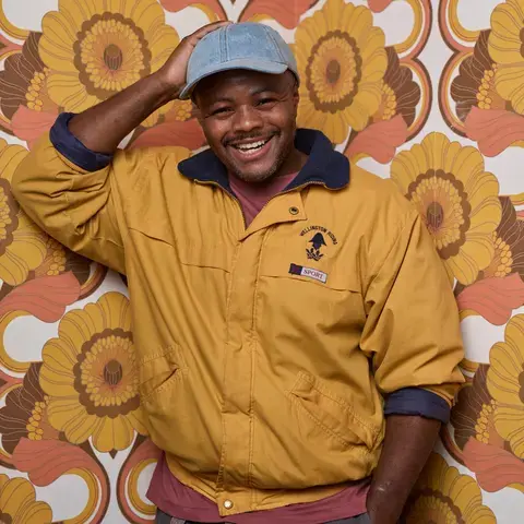 Chef Dom Taylor smiling against colourful wallpaper.