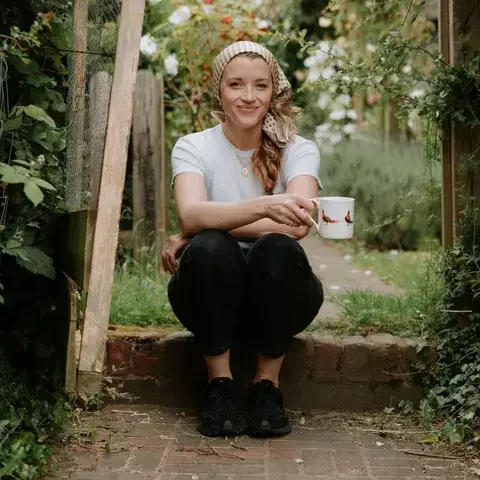 Lucy Sally Sommer sitting on a garden step, holding a mug.