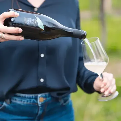 A person pouring a Feral drink into a wine glass.