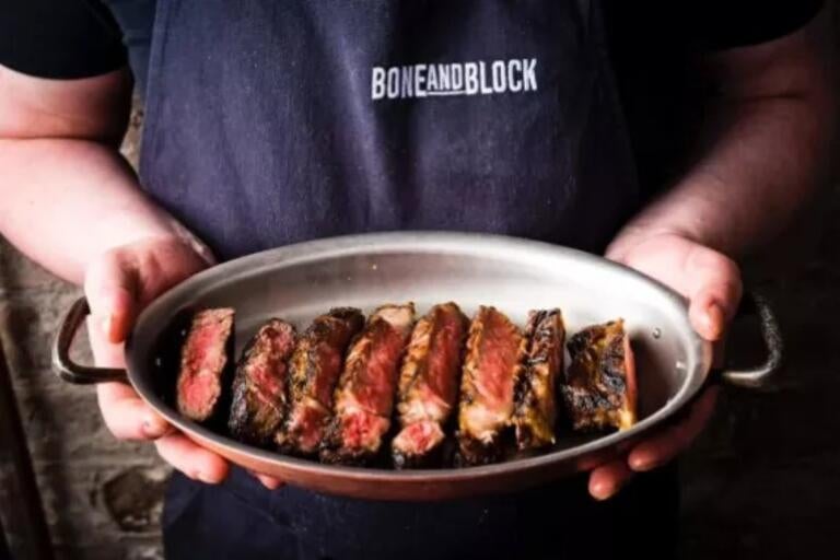 Person holding a dish of steak at Bone and Block.