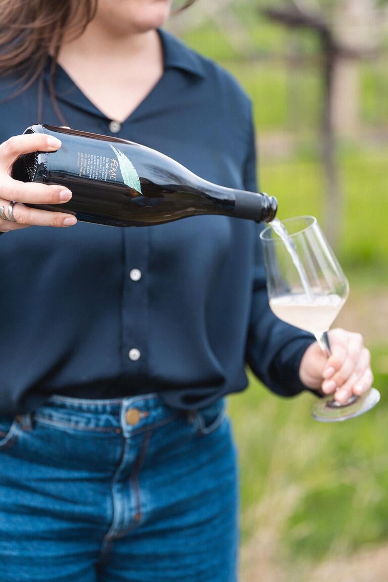 A woman pouring a Feral drink into a wine glass.