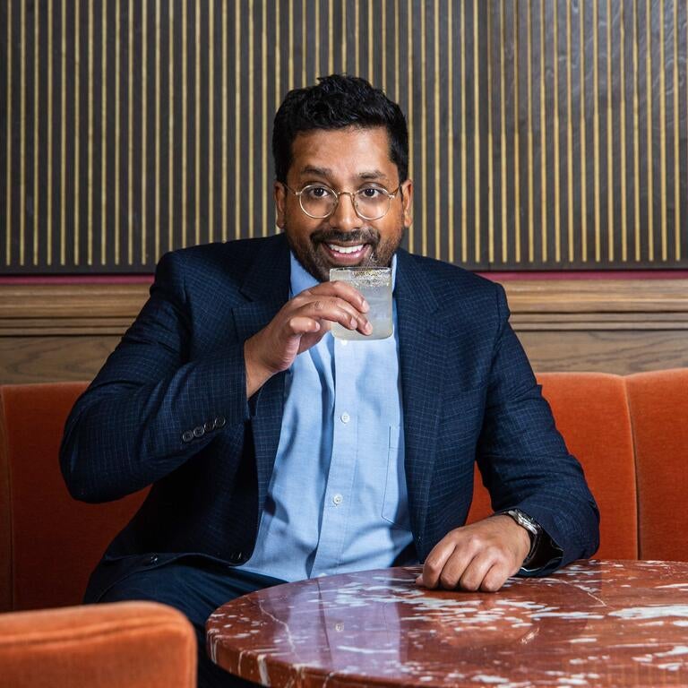 Ryan Chetiyawardana holding a drink at a bar table.