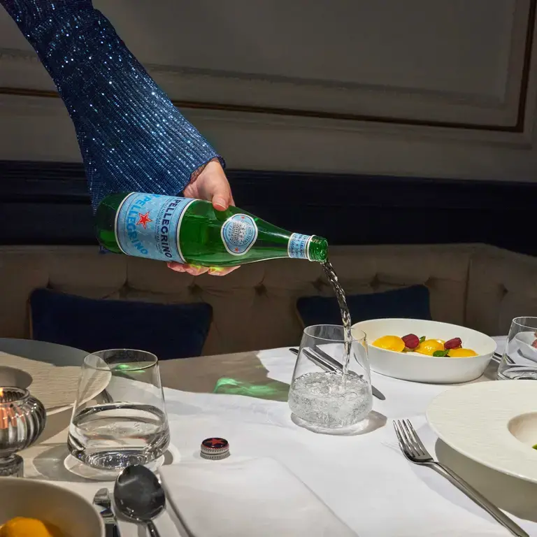 A girl pours S.Pellegrino water into a bottle.