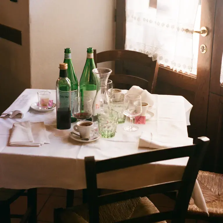 A restaurant table with empty water bottles, wine glasses and coffee cups.