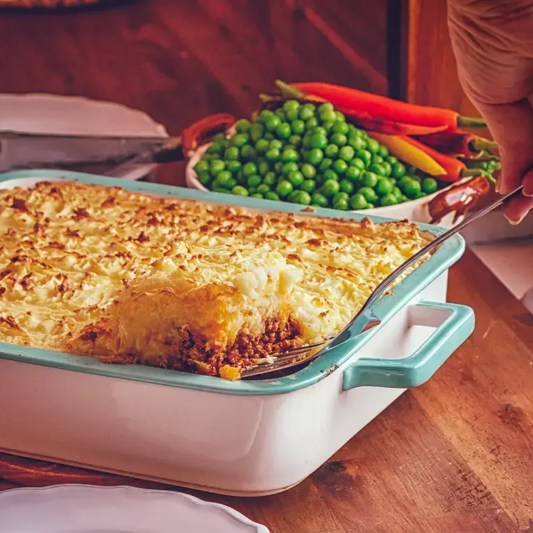 Someone spooning cottage pie from a casserole dish.