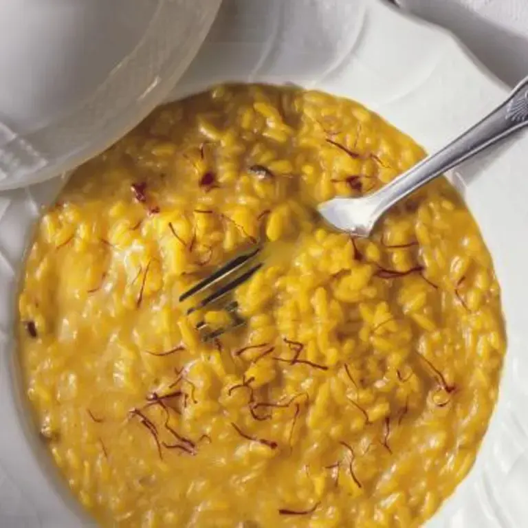 Risotto alla Milanese on a white plate with a fork.