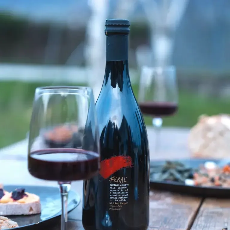 A bottle of Feral and a wine glass on a table.