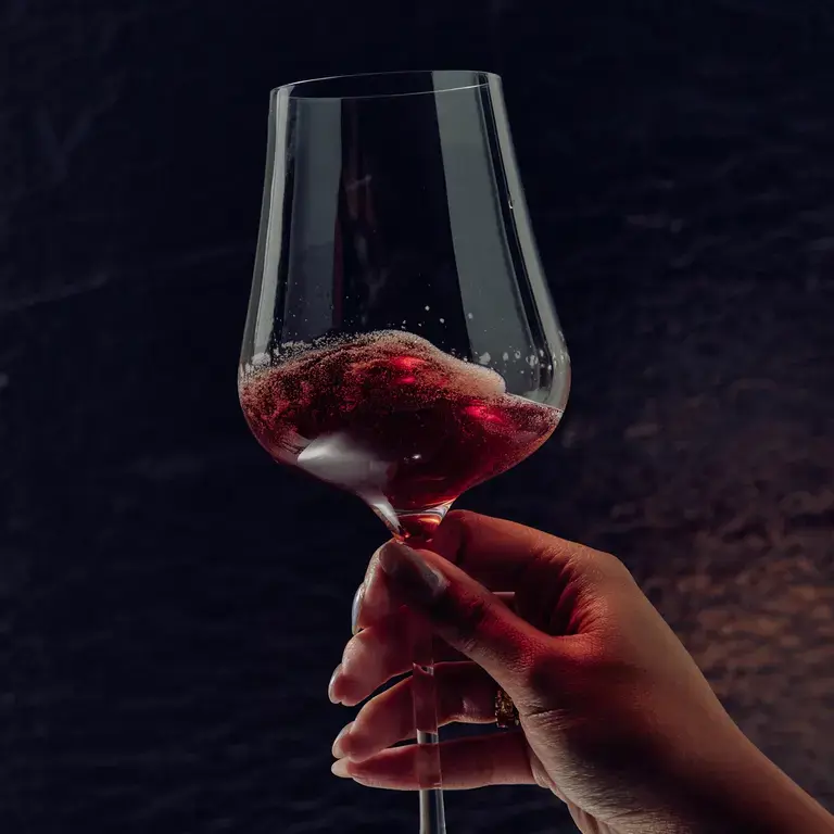 A woman's hand holding a wine glass of red Non, non-alcoholic beverage.