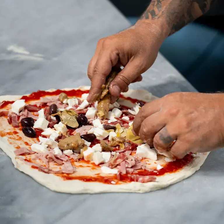Toppings being placed on a raw capricciosa pizza.