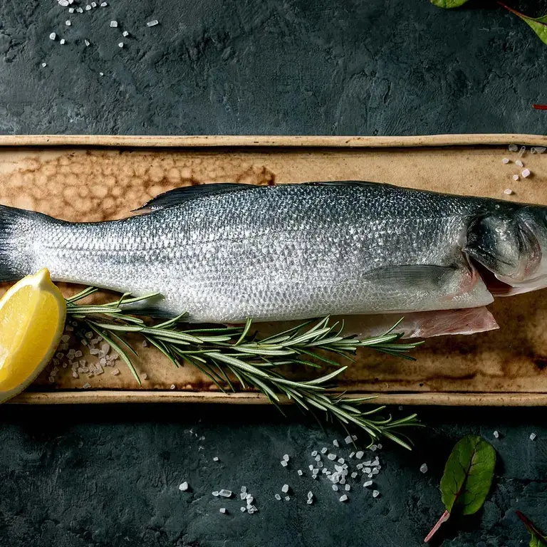Raw sea bass on ceramic plate with lemon, salt, herbs and leaves.