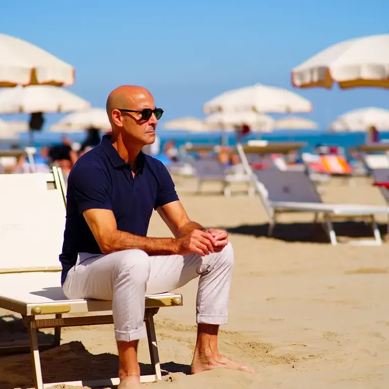 Stanley Tucci sat on a sun lounger on a sandy, sunny beach