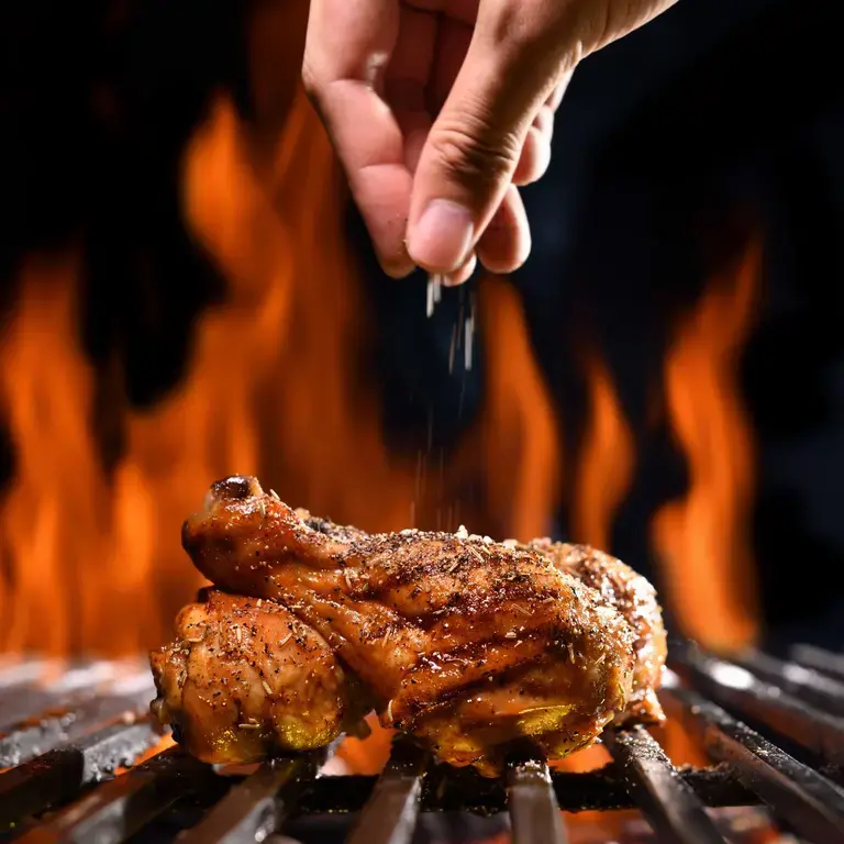 Chicken on the barbecue being seasoned.