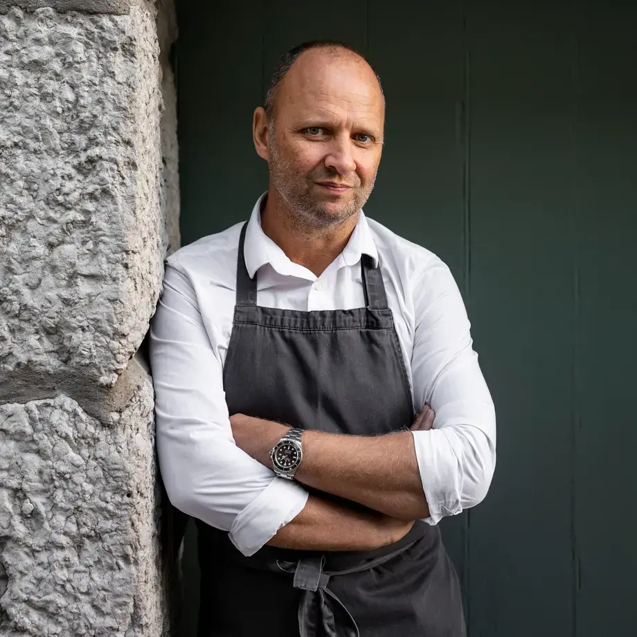 Chef Simon Rogan leaning against a stone wall.