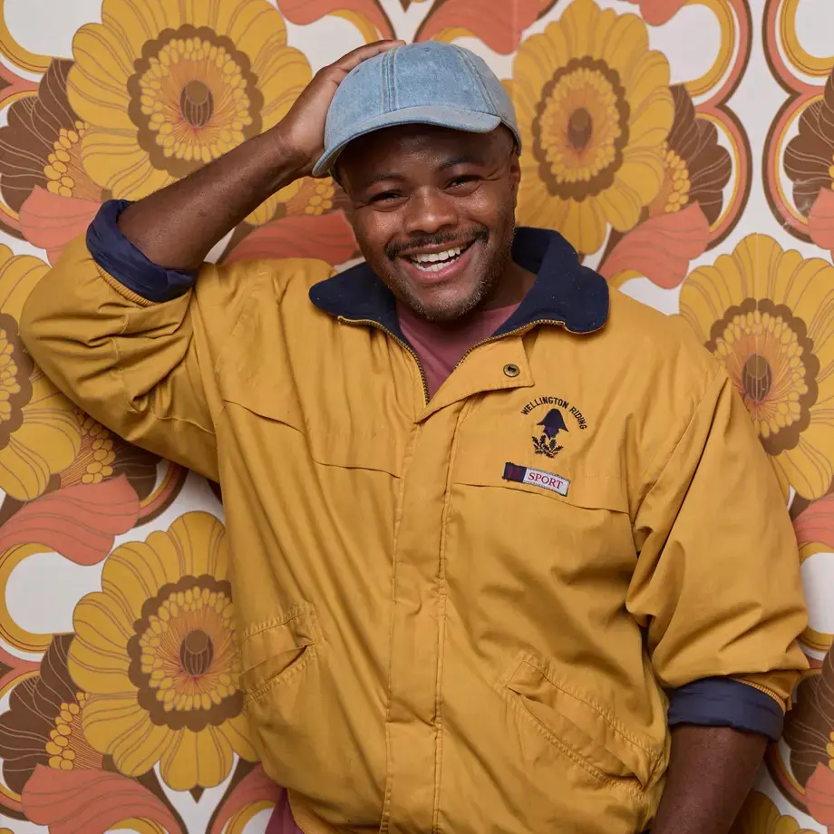 Chef Dom Taylor smiling against colourful wallpaper.