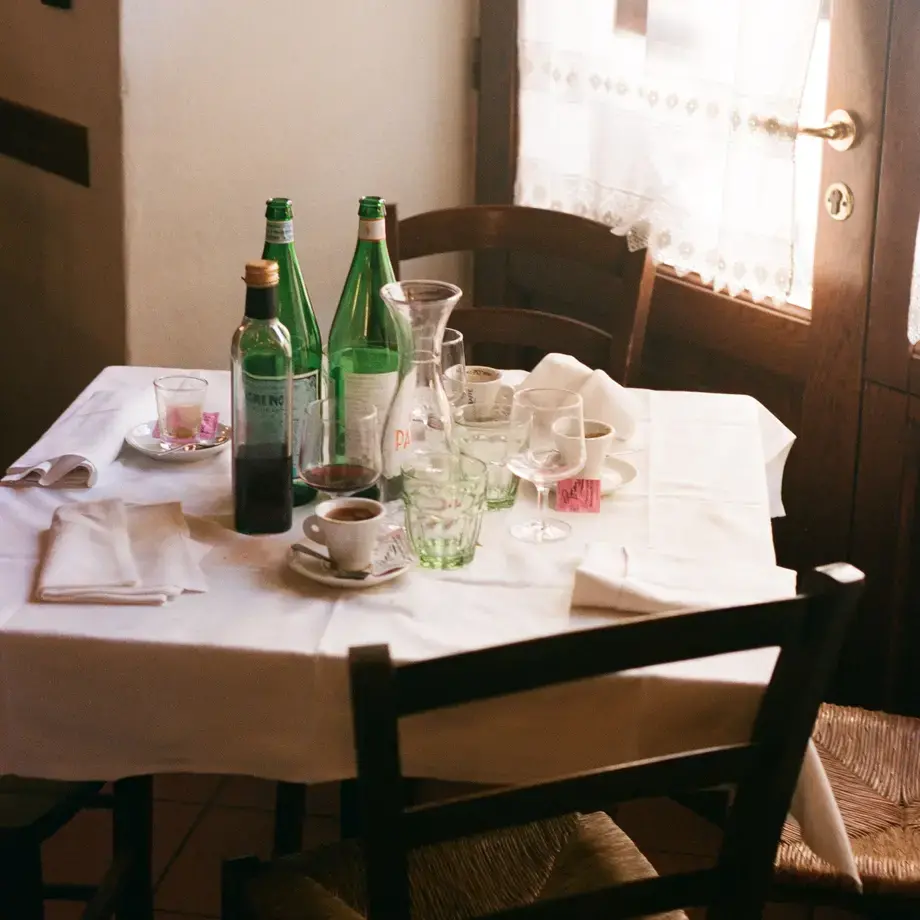 A restaurant table with empty water bottles, wine glasses and coffee cups.