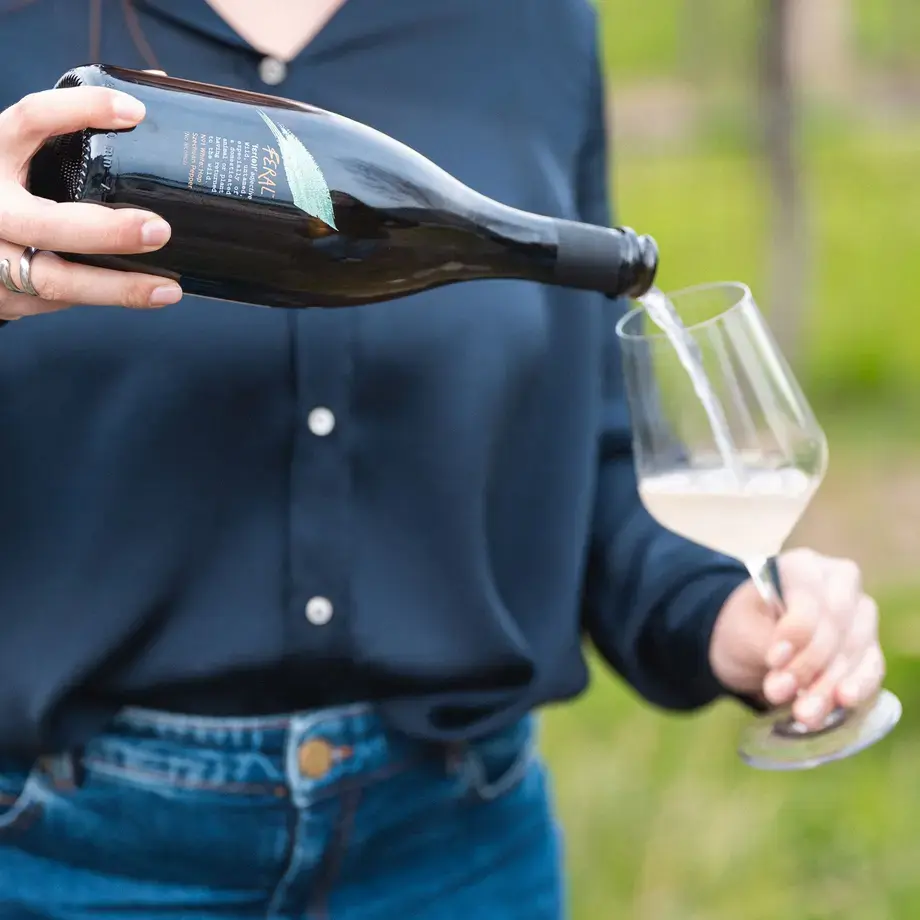 A person pouring a Feral drink into a wine glass.