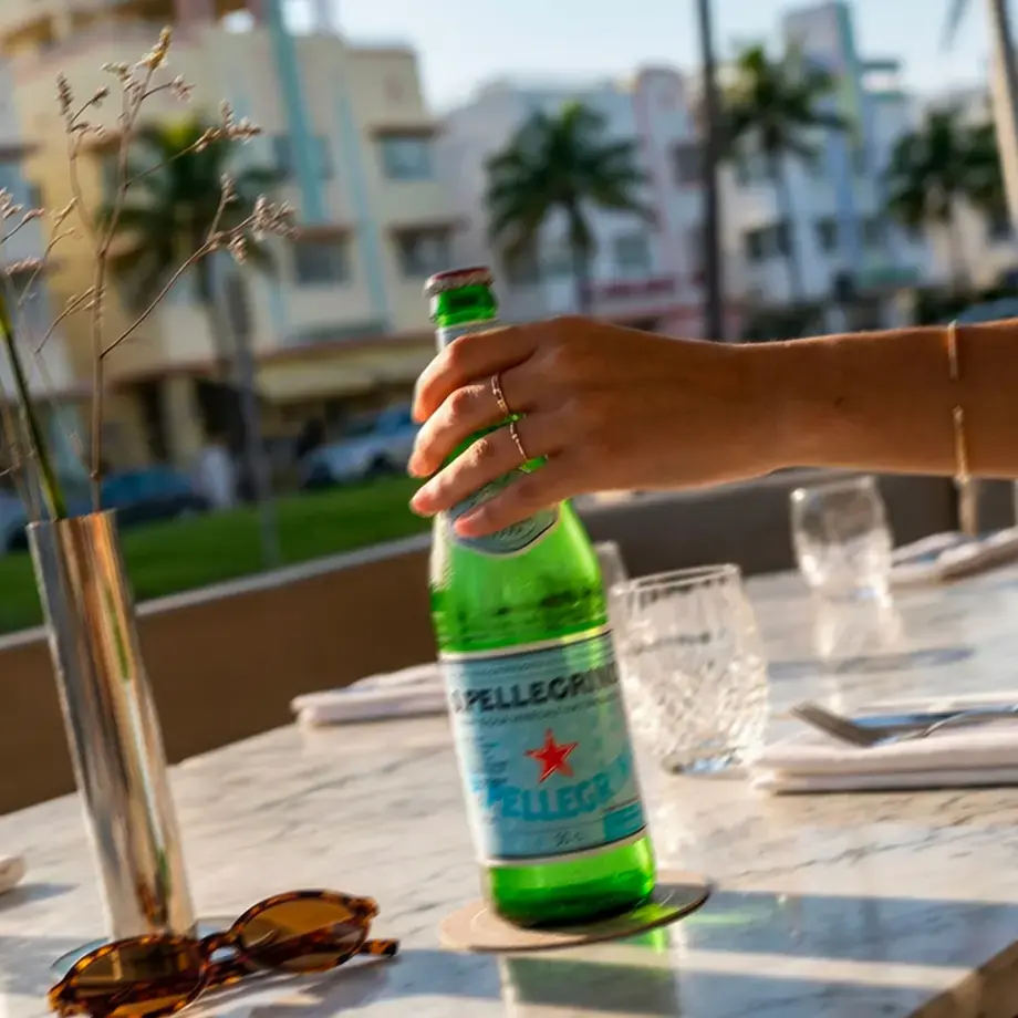 A hand holding a S.Pellegrino bottle on a Miami restaurant terrace.
