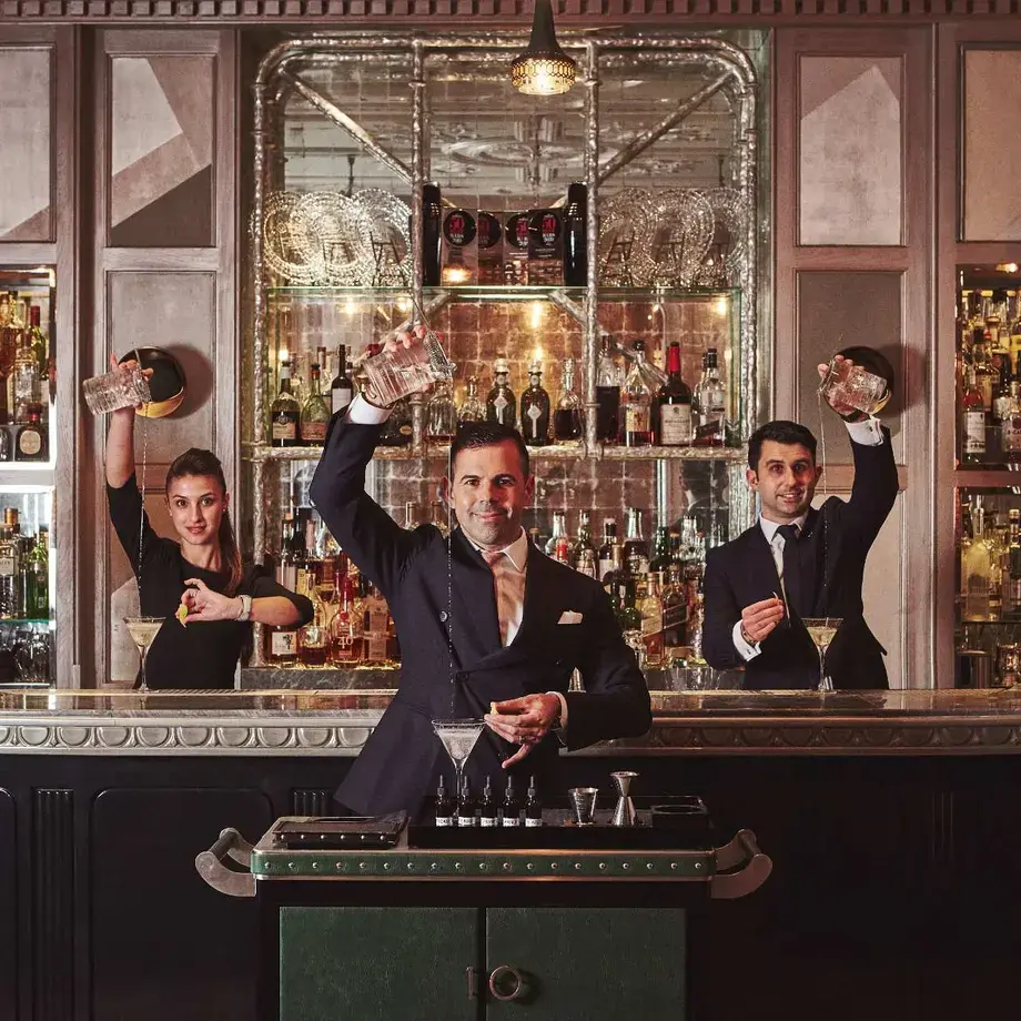 Three people mixing drinks at a bar.
