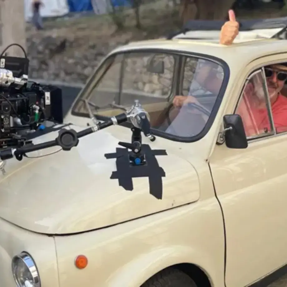 A man in a vintage white car with a video camera on the bonnet.