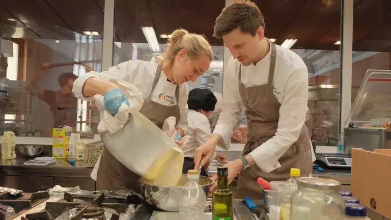 Chefs working together in a professional kitchen, pouring batter into a bowl