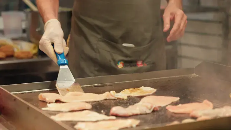 Chef grilling chicken breast slices on a professional griddle