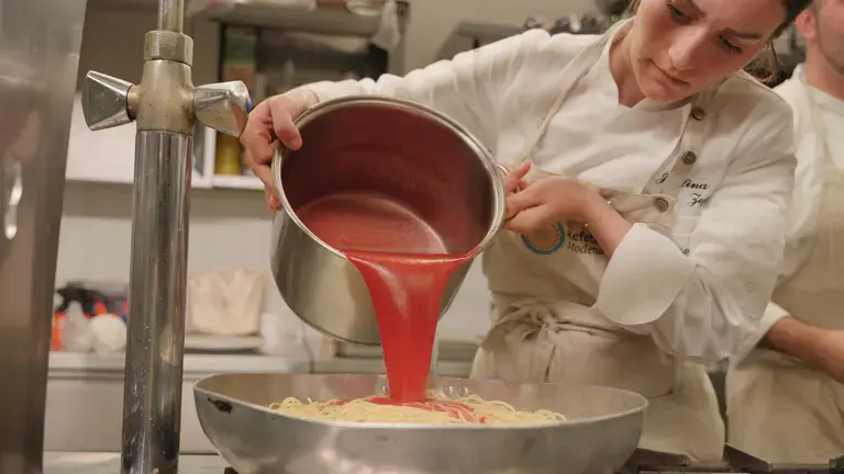 Chef seasoning spaghetti with tomato sauce