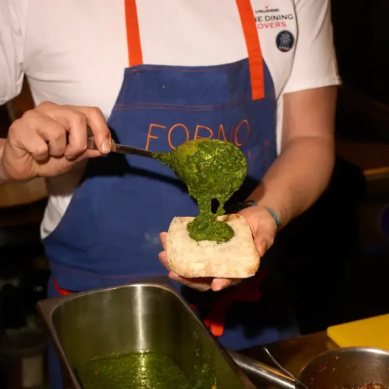 A chef spooning pesto onto bread at Forno.