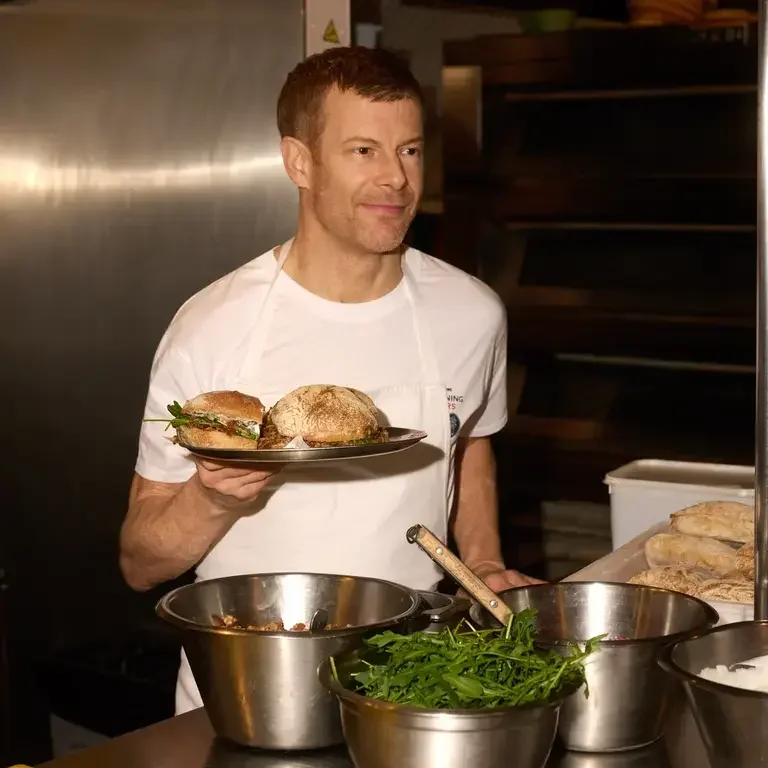 Chef Tom Aikens holding a sandwich on a metal plate.
