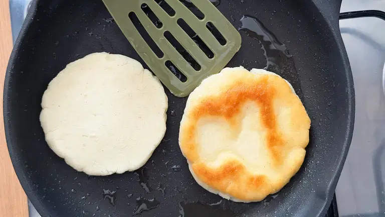 Pan-frying arepas until golden brown.
