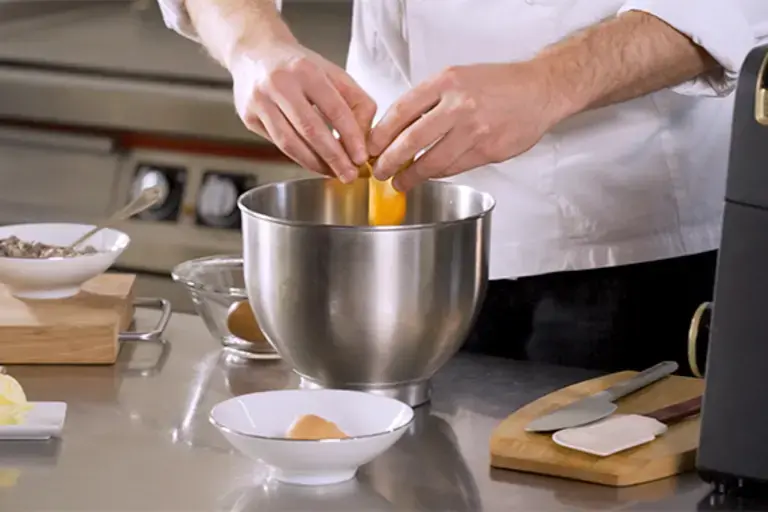 A chef cracks eggs into a bowl.