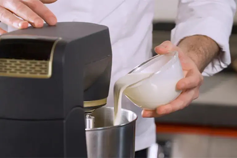 A chef pours cream into a mixing bowl.