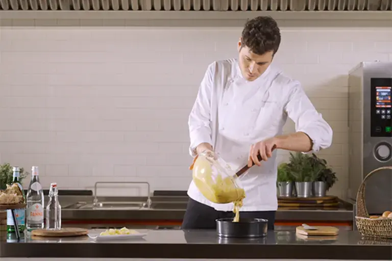 A chef pours cake mixture into a tin.