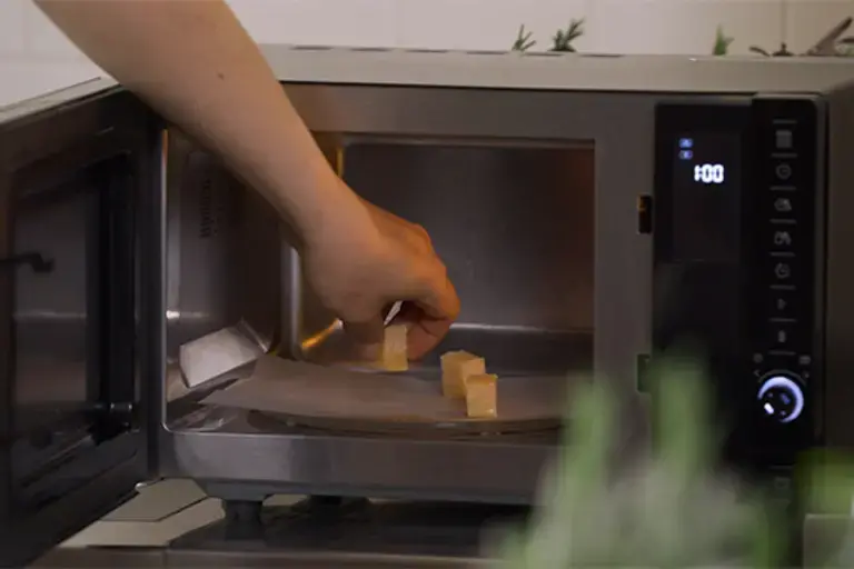 Chunks of cheese being placed into a microwave.
