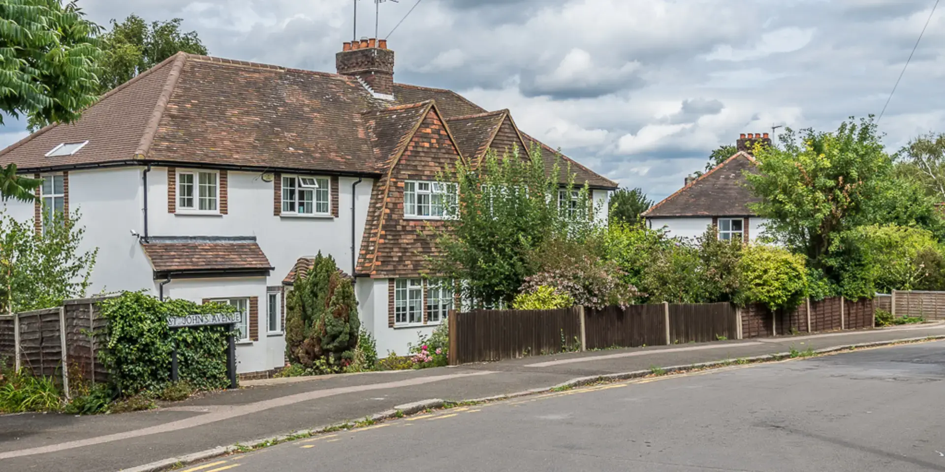 Charming British homes with brick chimneys and neatly trimmed gardens, set along St. Johns Avenue under a cloudy summer sky