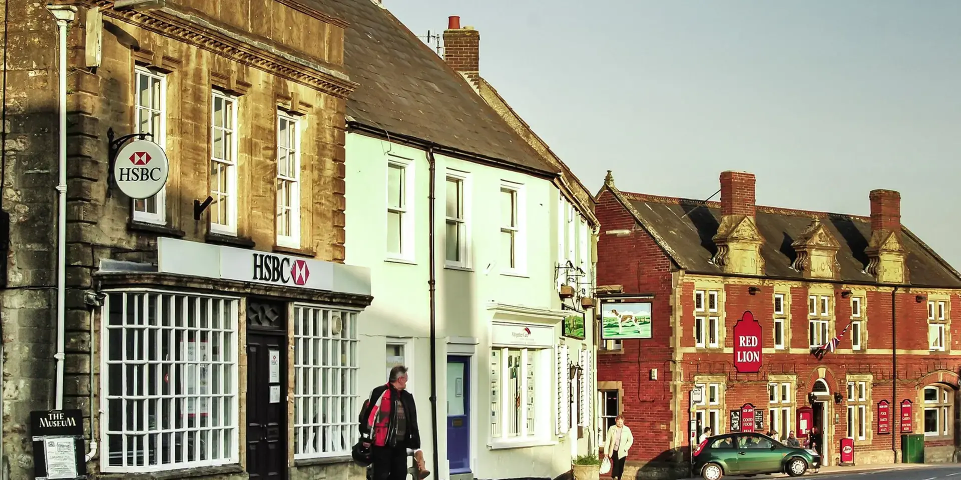 Historic town street with HSBC bank, pastel-colored buildings, and Red Lion pub in warm evening light