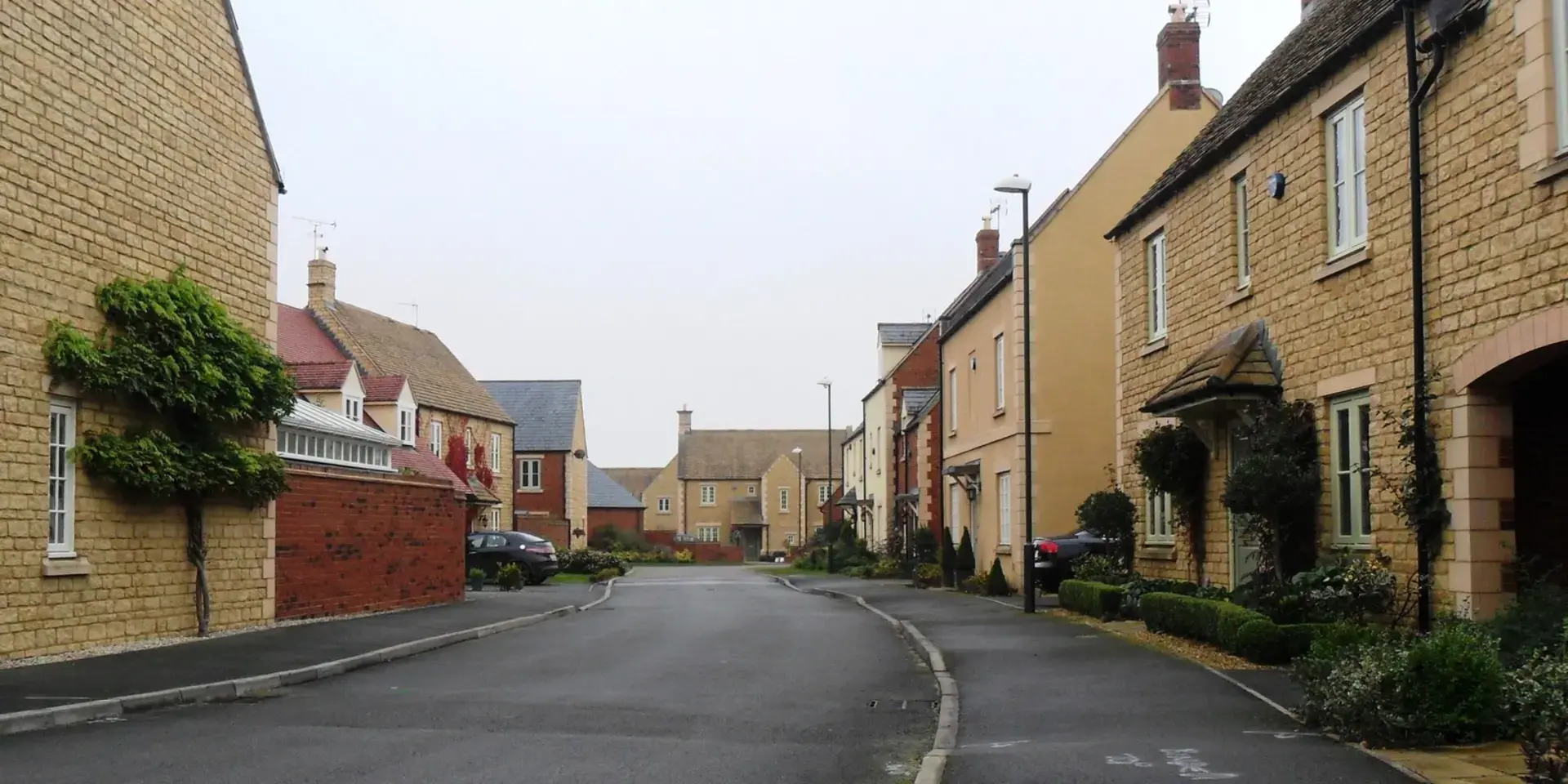 Stone houses line a quiet residential street with manicured greenery, creating a peaceful village ambiance