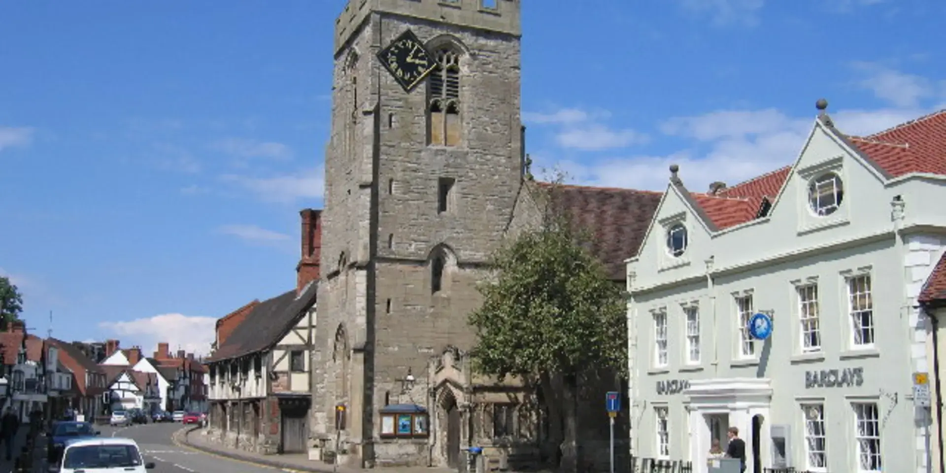 Historic church tower and village street in Henley-in-Arden, under a bright blue sky with charming architecture