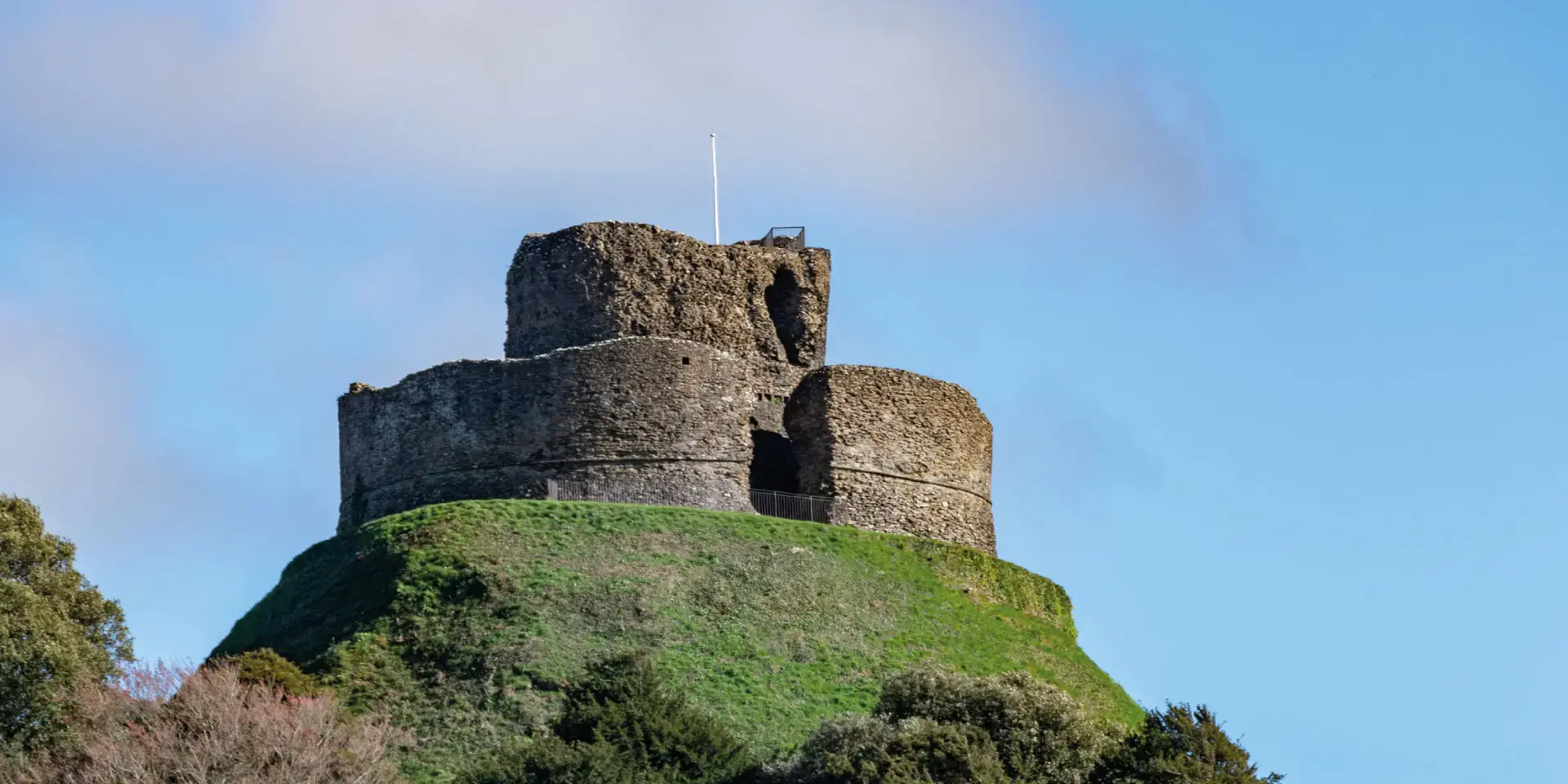 Historic stone ruins of Launceston Castle atop a grassy hill under a clear blue sky