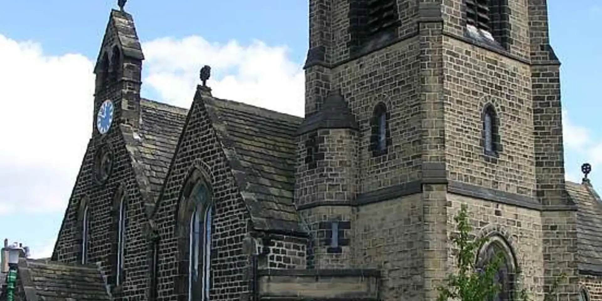 St John’s Church, a beautiful stone structure with a clock tower,surrounded by a manicured green lawn under a bright blue sky