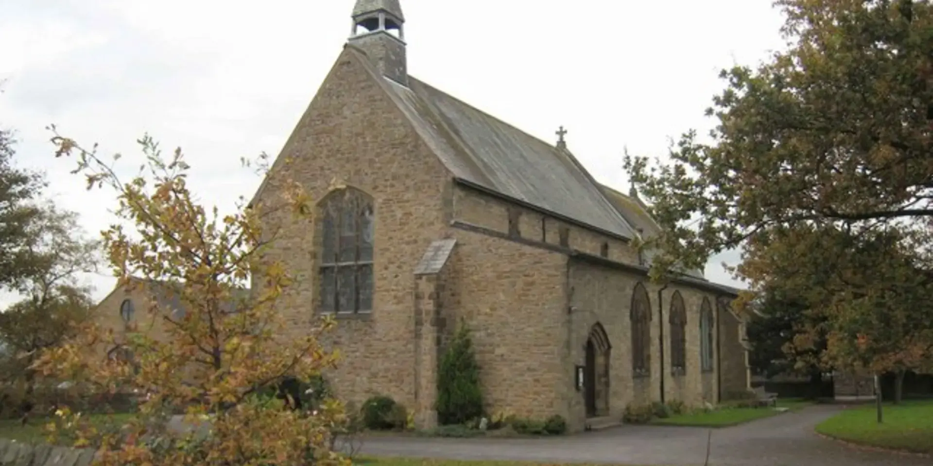 Stone-built St. Leonard’s Church with arched windows and a small bell tower, surrounded by autumn trees and greenery