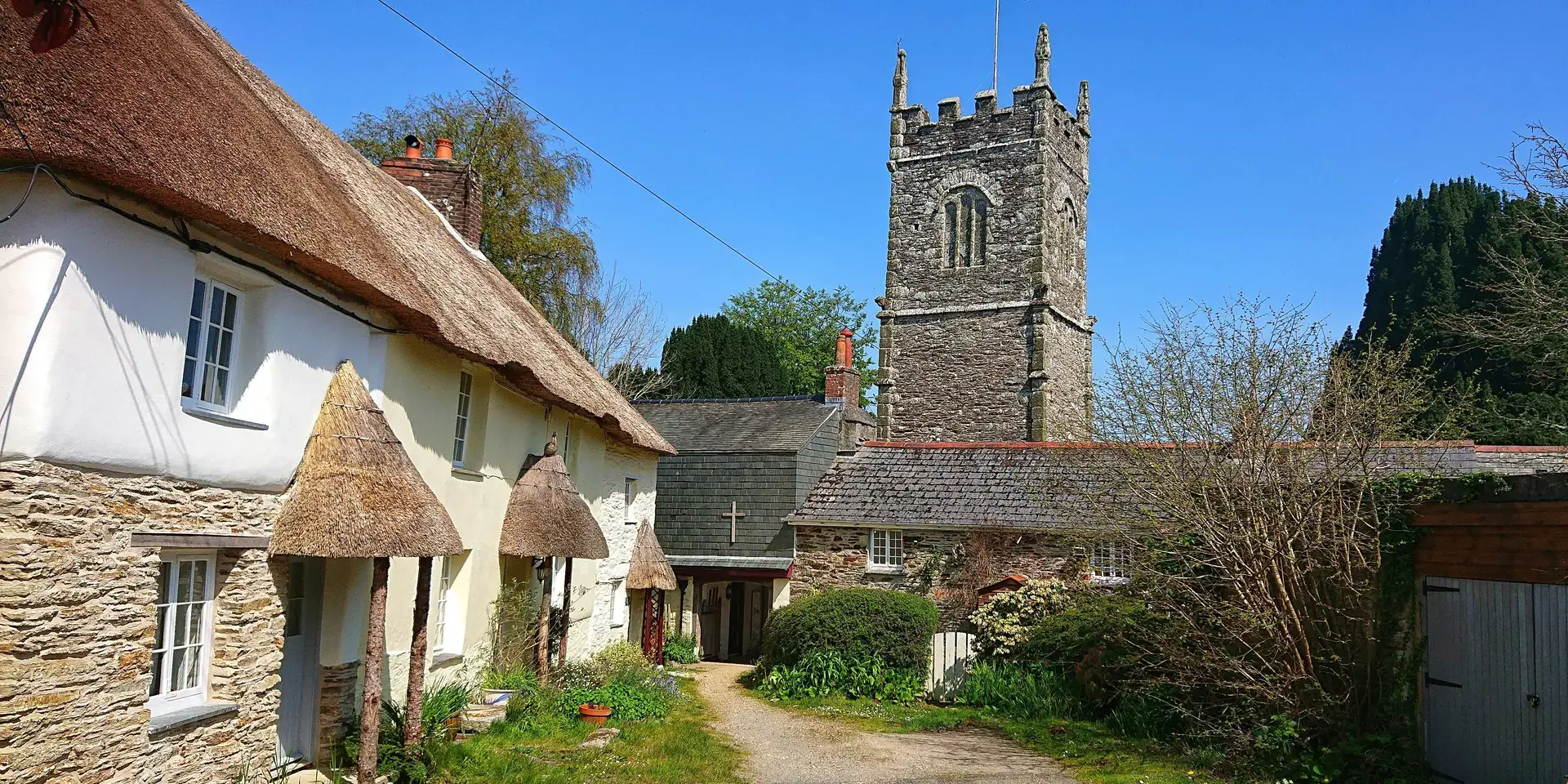 Traditional English village scene with thatched cottages and a historic stone church tower under a clear blue sky