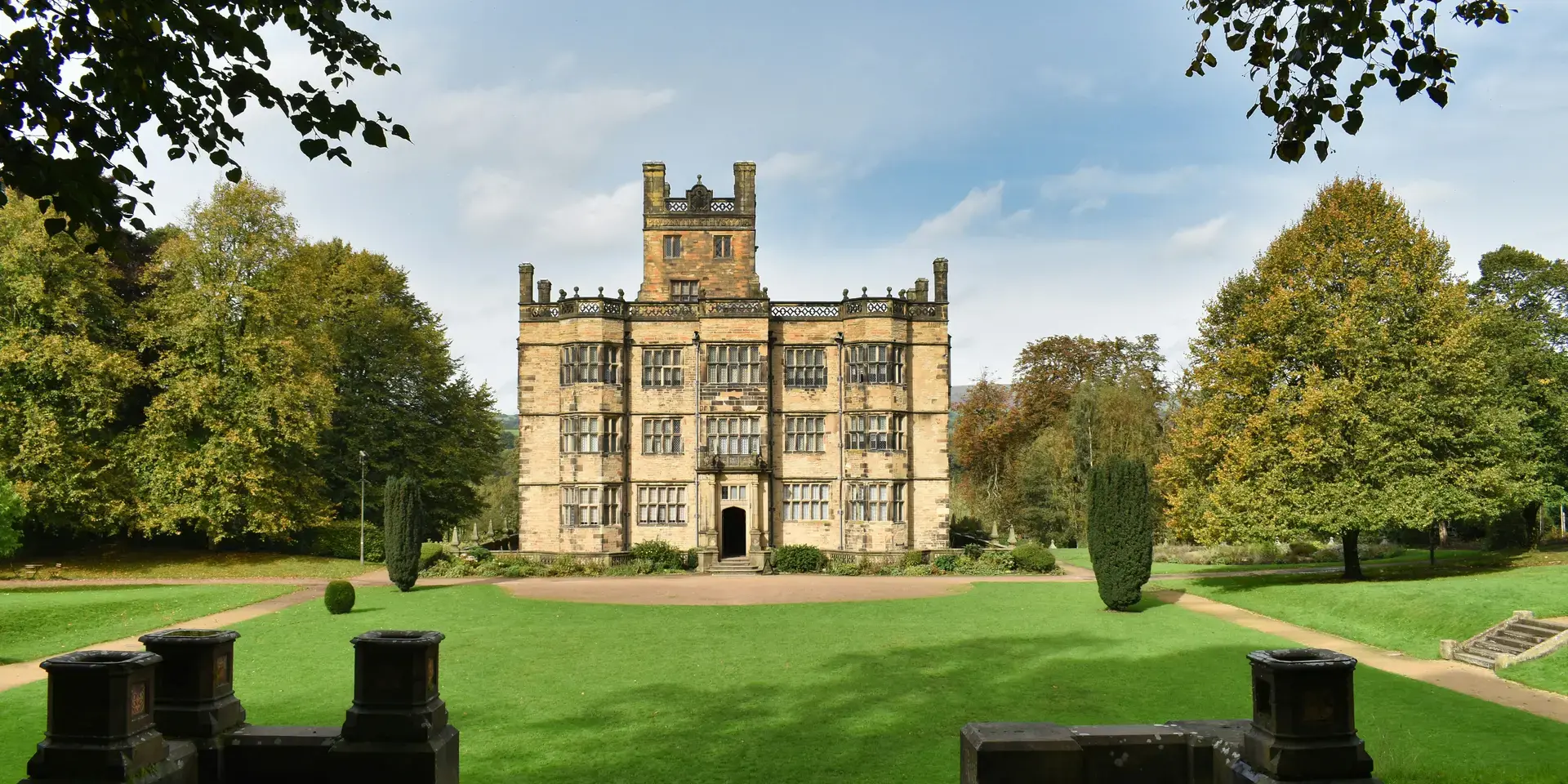 Historic stone mansion surrounded by a manicured lawn and tall trees, with intricate architecture and symmetrical windows