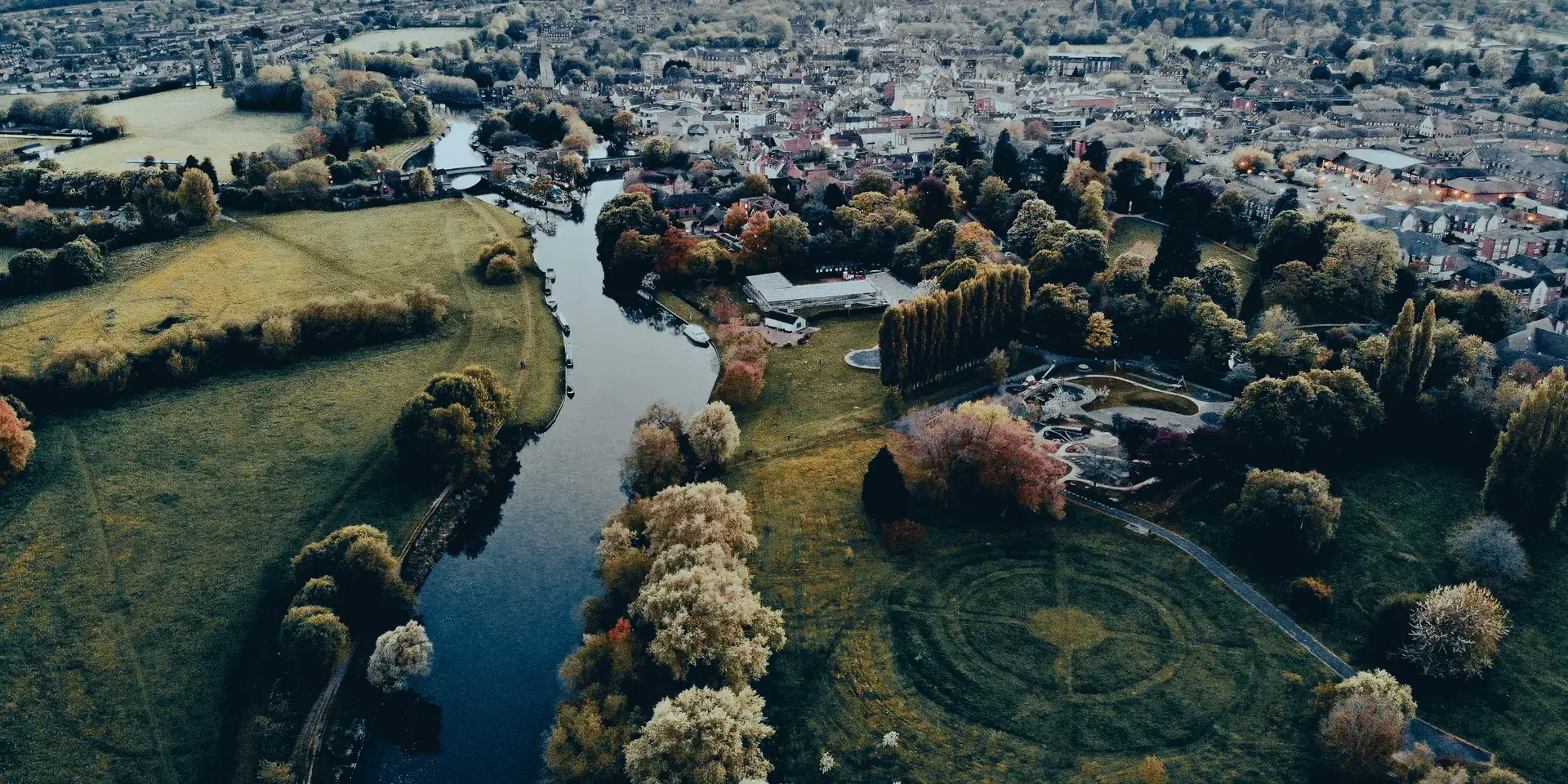 Aerial view of a river winding through a town, surrounded by green fields and trees, creating a peaceful and scenic landscape